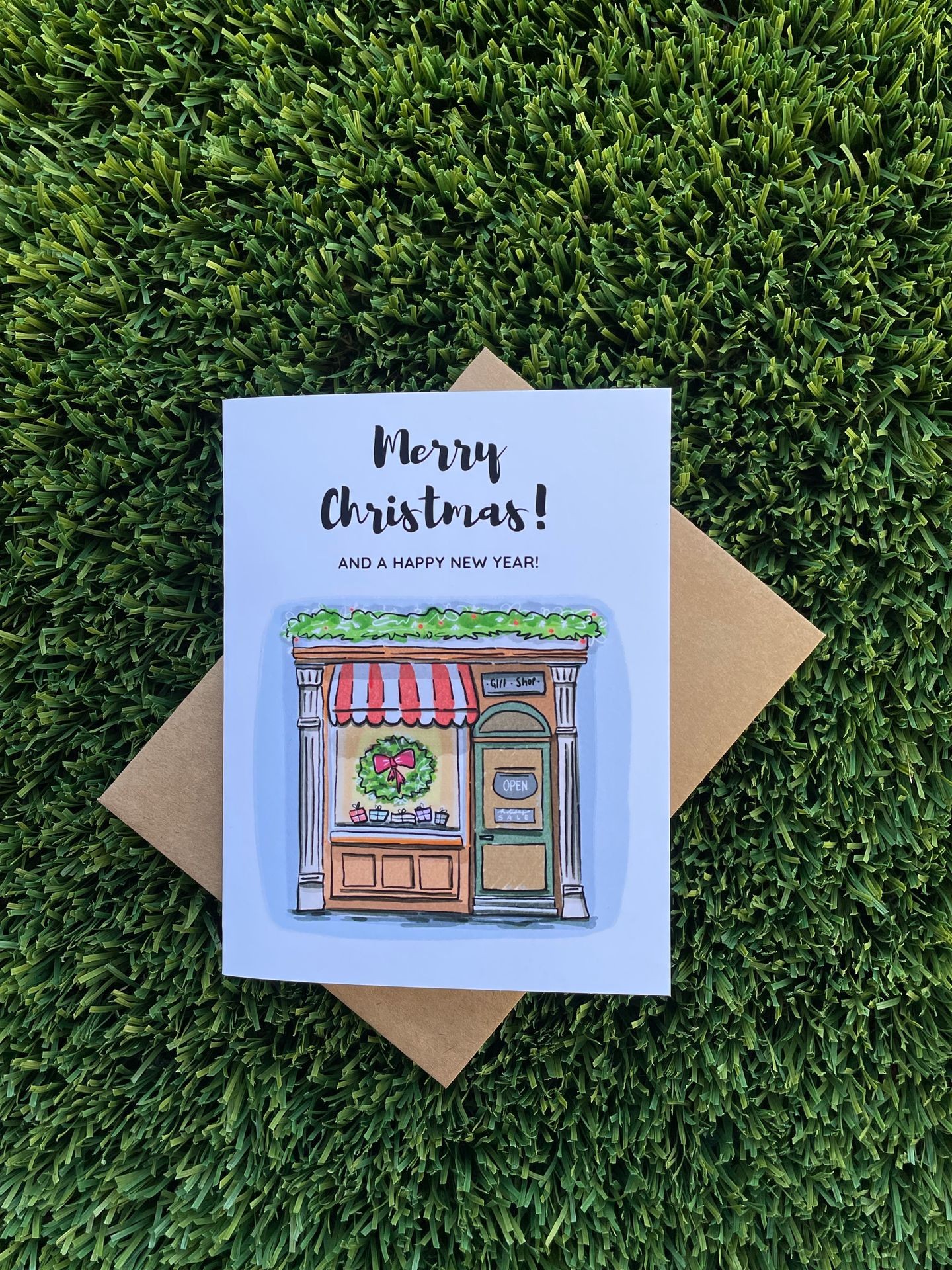 Christmas card with shop illustration and greetings on grass background.