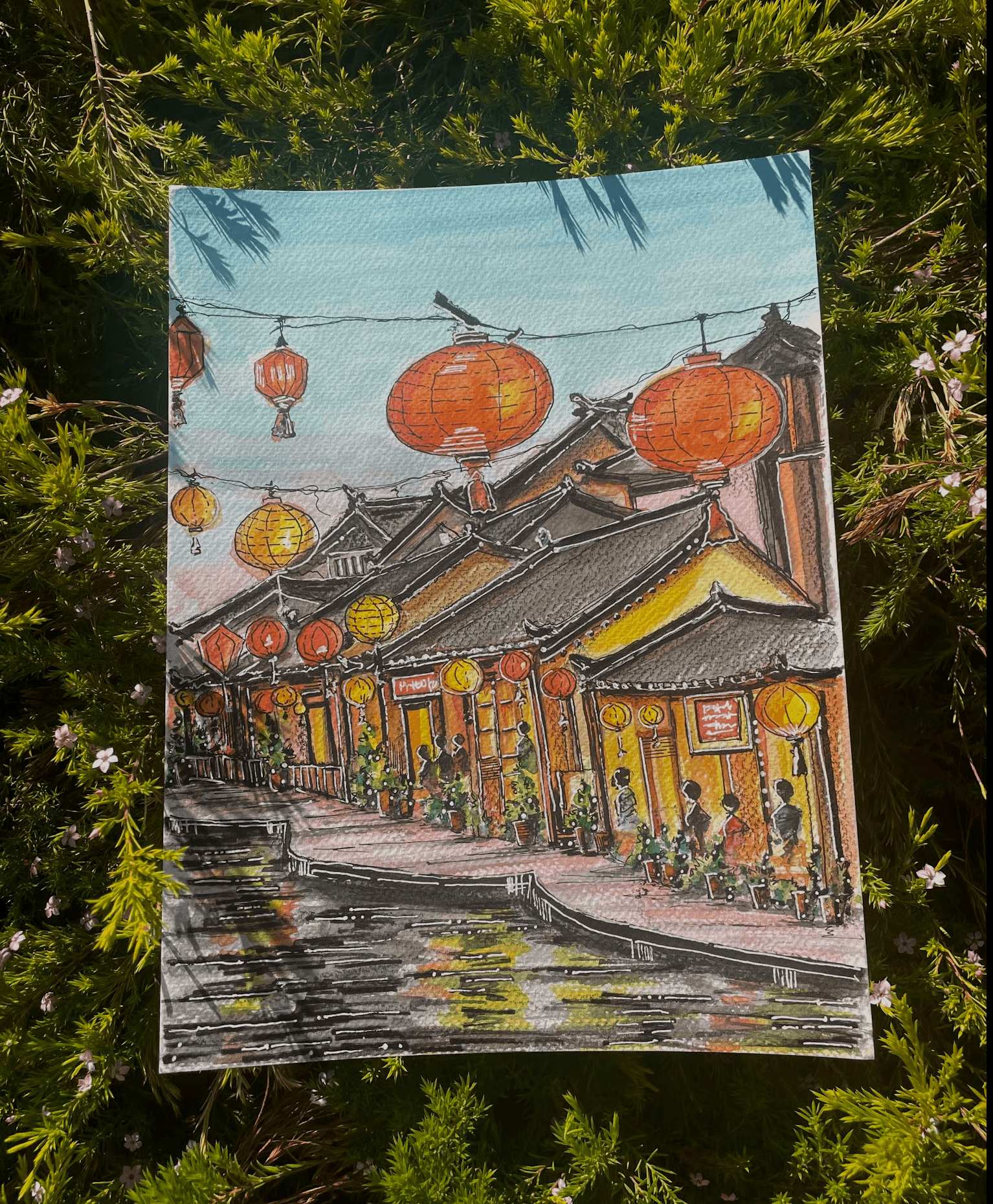 Colorful painting of a traditional street with lanterns and buildings, set against a grassy background.